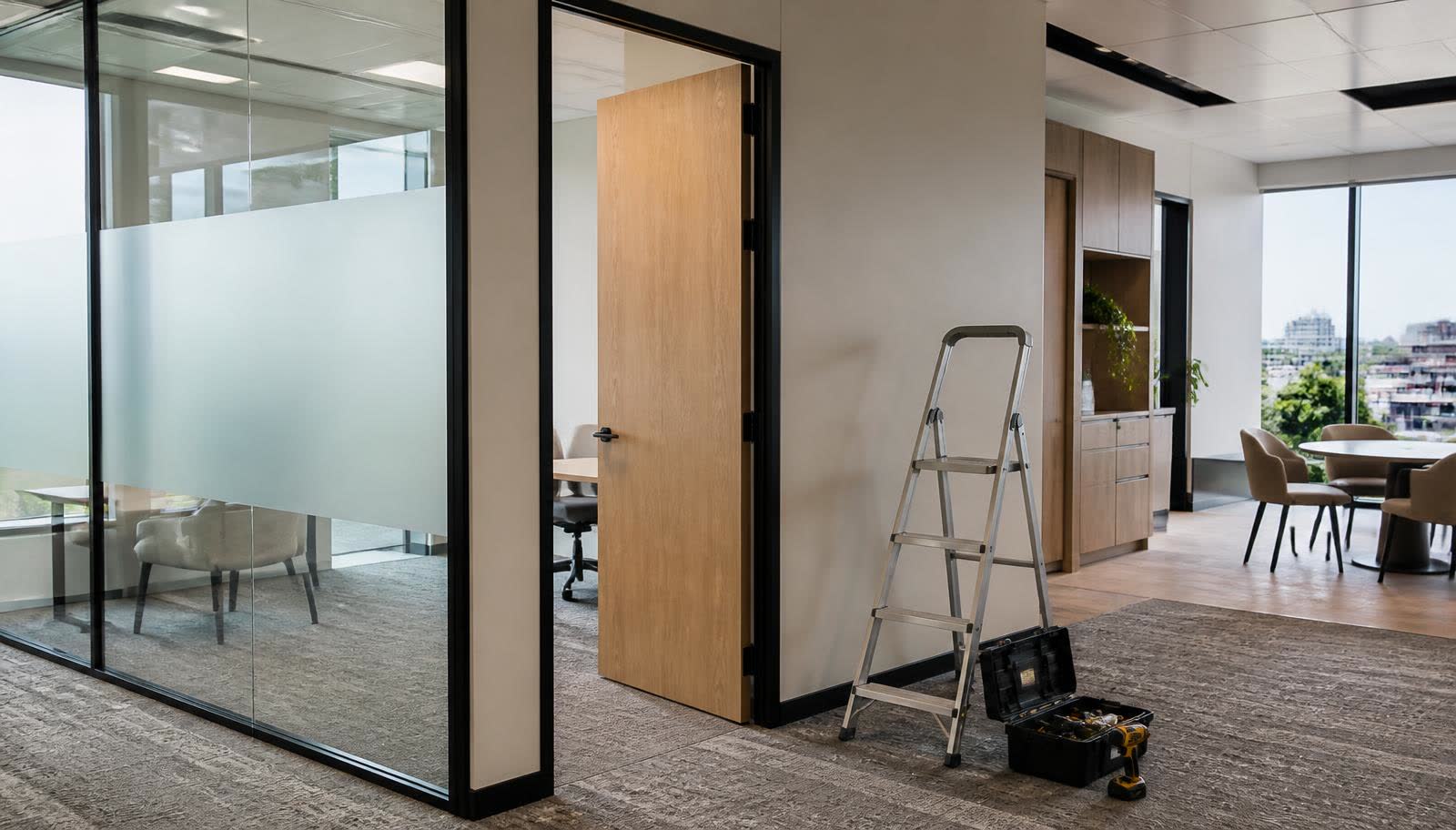 Modern office fit-out with glass partitions and a maintenance ladder beside a newly hung office door