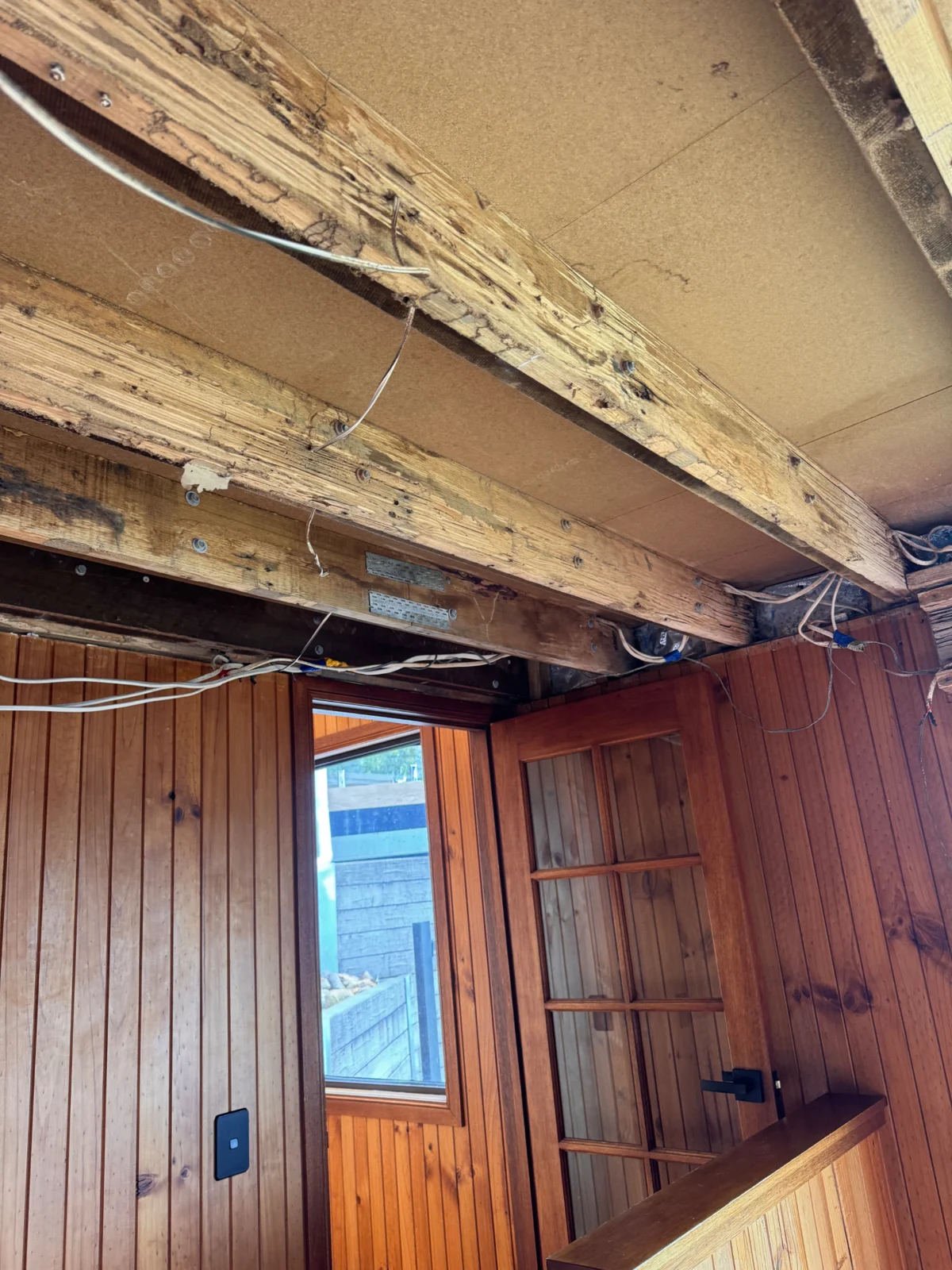 Termite-damaged ceiling beams exposed above timber wall panelling