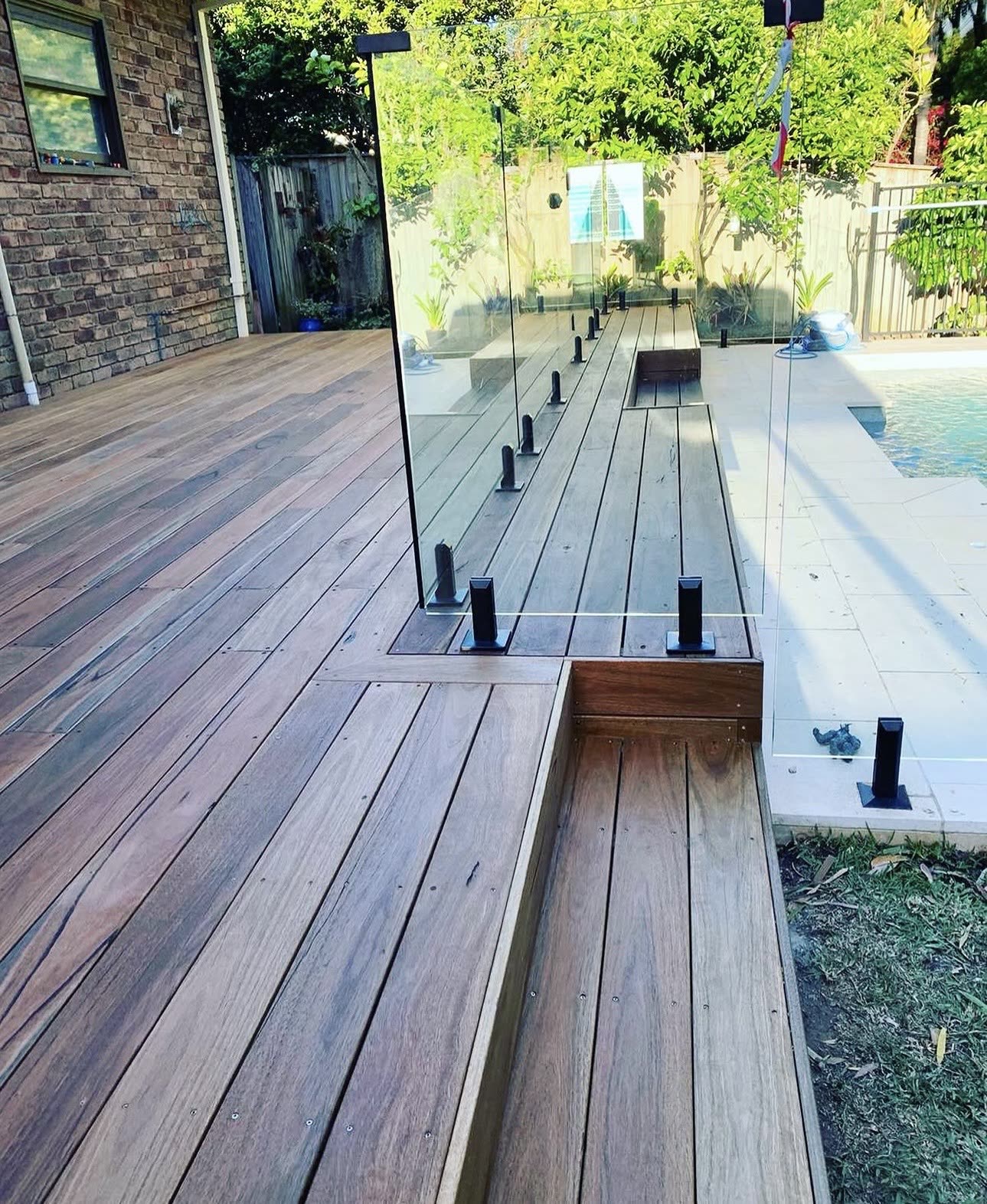 Hardwood pool deck with built-in step and frameless glass fencing