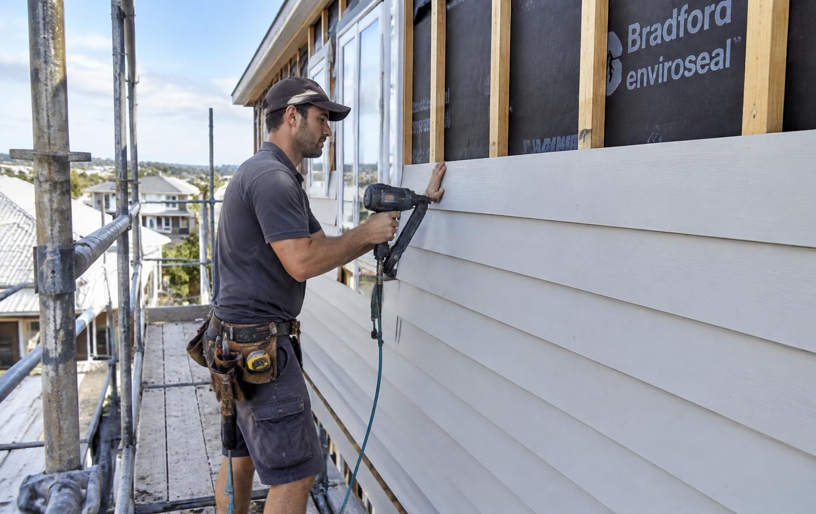 Carpenter fixing weatherboard cladding from scaffold